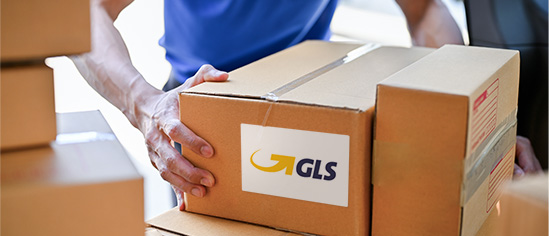 Person stellt Paket mit GLS-Versandetikett auf einen Stapel anderer Pakete. 